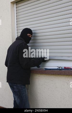 Einbrecher mit Schraubendreher, Brechstange und Taschenlampe auf einem Rollo Stockfoto