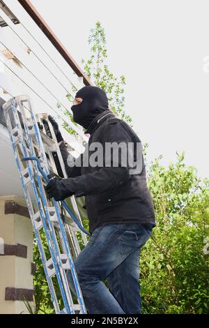 Einbrecher mit Brechstange und Taschenlampe auf einer Leiter auf einem Balkon Stockfoto