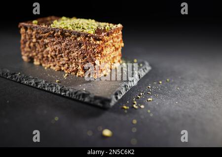 Schokoladenkuchen mit Walnüssen und Pistazien isoliert auf schwarzem Hintergrund. Gebäck aus hausgemachter Bäckerei Stockfoto