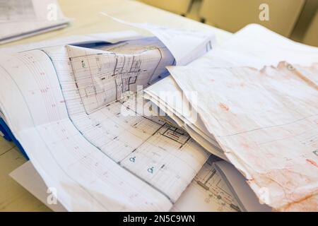 Masons Schreibtisch in einem Bürocontainer mit einem Haufen unordentlicher Architekturzeichnungen, Papierlayouts, Plänen. Stockfoto