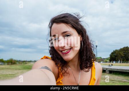 Selfie-Porträt einer jungen argentinischen Latina-Frau mit weißer Haut, gelb gekleidet und einem Reisenden, der mit einem süßen Lächeln und roten Lippen in die Kamera schaut Stockfoto