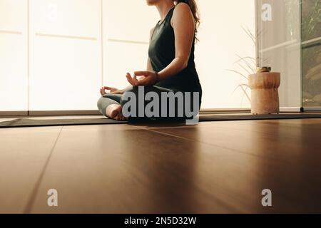 Reife Frau meditiert, während sie Hatha Yoga praktiziert. Eine unbekannte Frau, die eine Atemübung macht, während sie in lockerer Pose sitzt. Seniorin folgt Stockfoto