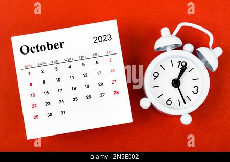 Oktober 2023 Monatliches Kalenderjahr mit Wecker auf rotem Hintergrund. Stockfoto