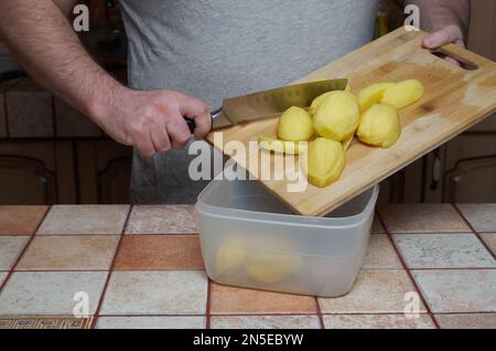 Kochen. Überführen von geschnittenen rohen Kartoffeln von einem Schneidebrett in einen Kunststoffbehälter Stockfoto