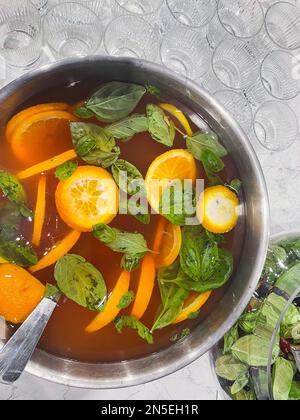 Schlagen Sie eine große Schüssel mit Orangen und Minze. Gekochter Zitrussaft. Trinken Sie aus nächster Nähe mit einer Vielzahl von Früchten. Orangefarbener alkoholischer Cocktail. Leere Brillen auf dem Stockfoto