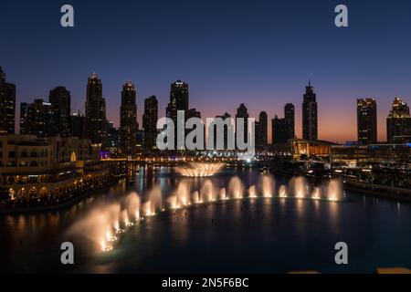 Dubai singende Brunnen bei Nacht Seeblick zwischen Wolkenkratzern. Moderne Architektur in der Dämmerung der Skyline der Stadt in der Innenstadt der Vereinigten Arabischen Emirate. Stockfoto