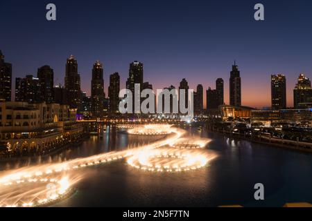 Dubai singende Brunnen bei Nacht Seeblick zwischen Wolkenkratzern. Moderne Architektur in der Dämmerung der Skyline der Stadt in der Innenstadt der Vereinigten Arabischen Emirate. Stockfoto