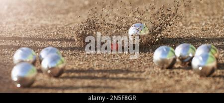 Petanque Ball Boules Schalen auf einem Staubboden, Foto beim Aufprall. Petanque-Spiel auf dem Boden. Bälle und ein kleiner Holzheber Stockfoto