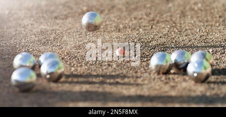 Petanque Ball Boules Schalen auf einem Staubboden, Foto beim Aufprall. Petanque-Spiel auf dem Boden. Bälle und ein kleiner Holzheber Stockfoto