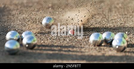 Petanque Ball Boules Schalen auf einem Staubboden, Foto beim Aufprall. Petanque-Spiel auf dem Boden. Bälle und ein kleiner Holzheber Stockfoto