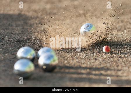 Petanque Ball Boules Schalen auf einem Staubboden, Foto beim Aufprall. Petanque-Spiel auf dem Boden. Bälle und ein kleiner Holzheber Stockfoto