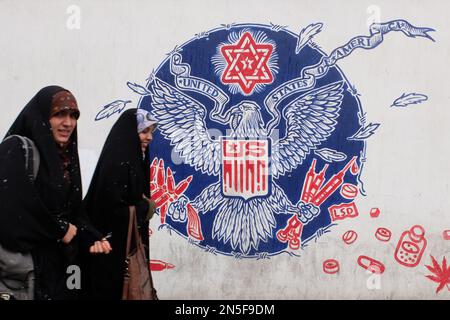 Teheran, Teheran, Iran. 9. Februar 2023. Zwei junge, getarnte iranische Frauen gehen am 09. Februar 2023 an einem Wandgemälde entlang der Mauer der ehemaligen US-Botschaft inmitten des Schnees in Teheran (Iran) vorbei. Der Leiter der Atomaufsicht der Vereinten Nationen unterstrich die Dringlichkeit, die diplomatischen Bemühungen zur Begrenzung des iranischen Atomprogramms wiederzubeleben, und erklärte, dass sich die Situation schnell verschlechtern könnte, wenn die Verhandlungen scheitern. (Kreditbild: © RouzbritFouladi/ZUMA Press Wire) NUR REDAKTIONELLE VERWENDUNG! Nicht für den kommerziellen GEBRAUCH! Kredit: ZUMA Press, Inc./Alamy Live News Stockfoto