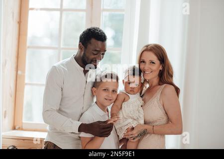 Gemischte Familie mit weißem Sohn und Tochter, die sich in einer gemütlichen Wohnung befindet. Ein afroamerikanischer Mann mit seiner hellhäutigen Frau Ki Stockfoto