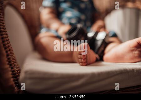 Ein kleines Mädchen in blauem Punktkleid hat positive Emotionen, wenn es auf einem Stock sitzt, hell und im Gesicht schattiert. afroamerikanisches Baby entspannt A Stockfoto