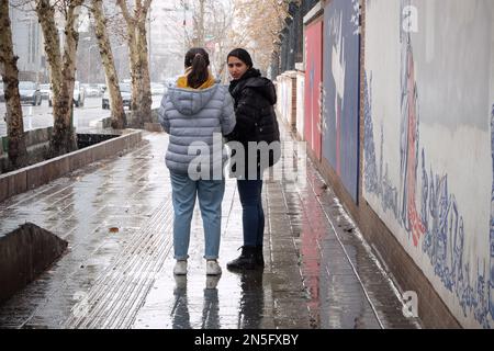 Teheran, Teheran, Iran. 9. Februar 2023. Zwei junge iranische Frauen, ohne ihre obligatorischen islamischen Kopftücher zu bedecken, stehen am 09. Februar 2023 inmitten des Schnees in Teheran, Iran, neben einem Wandgemälde der ehemaligen US-Botschaft. Der Leiter der Atomaufsicht der Vereinten Nationen unterstrich die Dringlichkeit, die diplomatischen Bemühungen zur Begrenzung des iranischen Atomprogramms wiederzubeleben, und erklärte, dass sich die Situation schnell verschlechtern könnte, wenn die Verhandlungen scheitern. (Kreditbild: © RouzbritFouladi/ZUMA Press Wire) NUR REDAKTIONELLE VERWENDUNG! Nicht für den kommerziellen GEBRAUCH! Kredit: ZUMA Press, Inc./Alamy Live News Stockfoto