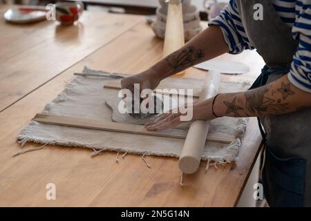 Nahaufnahme der Hand einer kreativen Künstlerin, die ein Meisterwerk aus rohem Ton mit Holzrollen kreiert Stockfoto