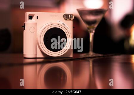 Mechelen, Belgien - 10. Dezember 2022: Nahaufnahme einer polaroid-Instax-Fotokamera, die auf einer Holzfläche steht, mit einem Cocktailglas daneben und t Stockfoto