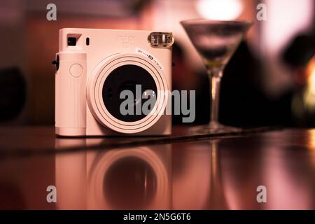 Mechelen, Belgien - 10. Dezember 2022: Ein Porträt einer instax-polaroid-Fotokamera auf einer Holzfläche mit einem Cocktailglas daneben und t Stockfoto