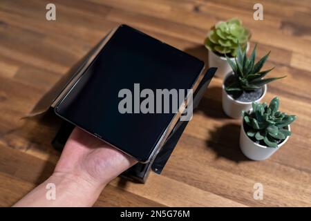 Samsung Galaxy Z Fold 4 in grau-grüner Farbe. Ein Mann packt das neue Handy aus. Stockfoto