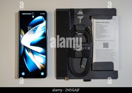 Samsung Galaxy Z Fold 4 in grau-grüner Farbe. Das Gerät befindet sich in der geschlossenen Position. Originalverpackung an der Seite. Stockfoto