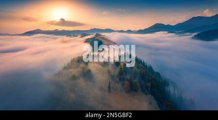 Atemberaubender Sonnenaufgang in den Karpaten. Atemberaubender Blick von der fliegenden Drohne auf das neblige Tal am Morgen. Über dem Berg breitet sich dichter Nebel aus Stockfoto