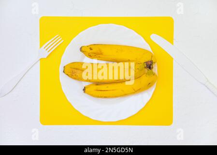 Reife gelbe Bananen auf einem weißen Teller. Layout, Ansicht von oben. Stockfoto