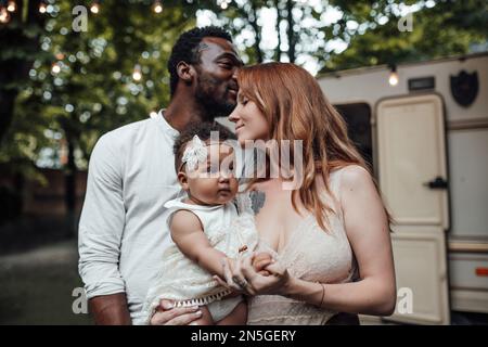 Gemischte Familien mit dunkelhäutigen Kleinkindern verbringen Zeit mit Umarmungen und Küssen im Campingpark. Ein afroamerikaner, seine schöne Frau und li Stockfoto