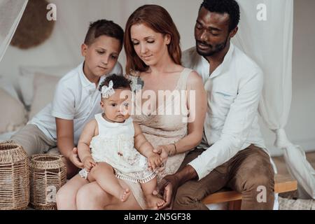Gemischte Familie mit weißem Sohn und Tochter, die sich in einer gemütlichen Wohnung befindet. Ein afroamerikanischer Mann mit seiner hellhäutigen Frau Ki Stockfoto
