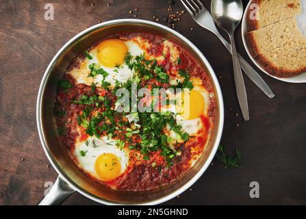 Leckeres und gesundes Shakshuka, nahöstliches Omelett in einer Bratpfanne. Leckeres Rührei, gekocht in scharfer Tomatenpfeffersauce auf einem rauen Holztisch. Stockfoto