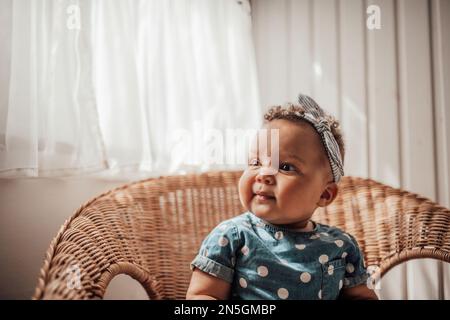 Ein kleines Mädchen in blauem Punktkleid hat positive Emotionen, wenn es auf einem Stock sitzt, hell und im Gesicht schattiert. afroamerikanisches Baby entspannt A Stockfoto