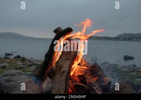 Das einladende Lagerfeuer am Strand im Sommer bringt schöne Erinnerungen zurück. Spaß und Spaß am See. Stockfoto