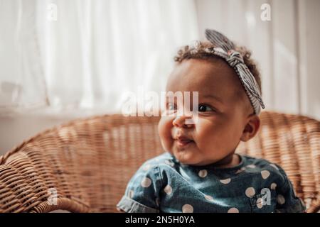 Ein kleines Mädchen in blauem Punktkleid hat positive Emotionen, wenn es auf einem Stock sitzt, hell und im Gesicht schattiert. afroamerikanisches Baby entspannt A Stockfoto