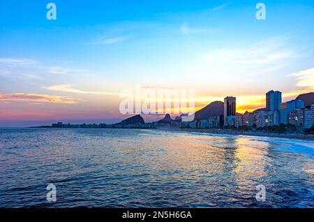 Sonnenuntergang am Copacabana-Strand in Rio de Janeiro mit Licht hinter den Gebäuden und Hügeln Stockfoto