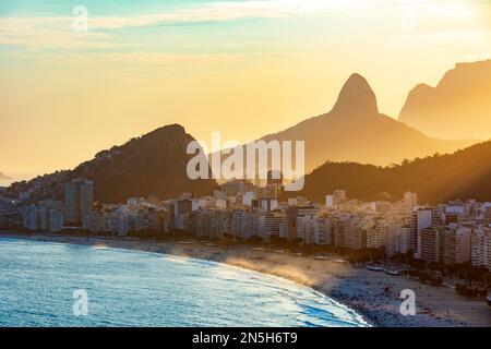 Sonnenuntergang am Copacabana Strand in Rio de Janeiro mit Licht hinter den Gebäuden und Hügeln Stockfoto