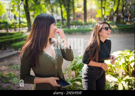 Zwei junge lateinische Freundinnen, die im Wald spazieren gehen Stockfoto