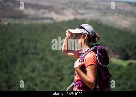 Eine Wanderin, die an einem sonnigen Tag ihre Mütze aufsetzt. Stockfoto