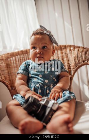 Ein kleines Mädchen in blauem Punktkleid hat positive Emotionen, wenn es auf einem Stock sitzt, hell und im Gesicht schattiert. afroamerikanisches Baby entspannt A Stockfoto