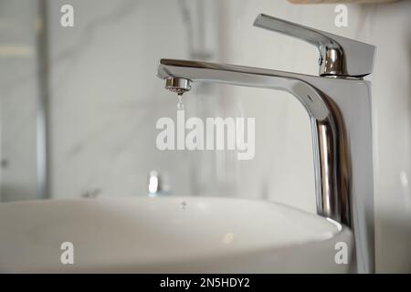 Wassertropfen fällt aus dem Wasserhahn auf verschwommenem Hintergrund, Nahaufnahme Stockfoto