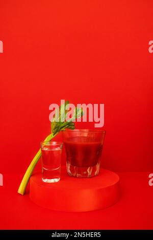 Ein Glas roter Cocktail mit Grün auf dem Podium. Stilvolles alkoholisches Tomatengetränk Bloody Mary auf rotem Hintergrund. Köstliches Getränkekonzept. Kopie SPA Stockfoto