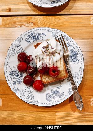 Tellermuster mit einem süßen Dessert drauf. Leckere Scheiben von Kuchen mit Kirschen, Beeren und Sahne auf einem wunderschönen Teller mit blauer Malerei und Flowe Stockfoto