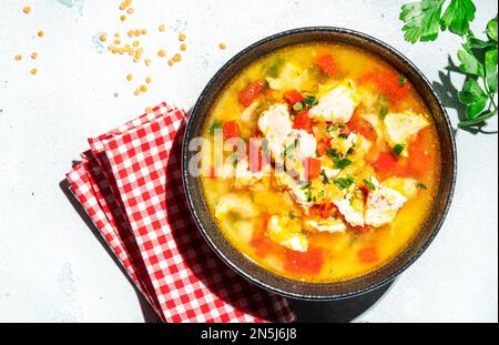 Wärmende Herbstsuppe mit roten Linsen, Hühnerfilet, Gemüse, Gewürzen und Paprika, Gemüsefutter. Weißer Tisch, hartes Licht mit Blattschatten, Spitzenspiel Stockfoto