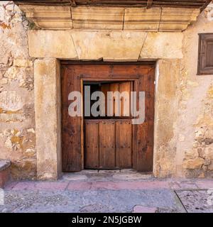 Alte Holztür, die sich in zwei Teilen in den Steinhäusern des mittelalterlichen Dorfes Pedraza, Segovia, öffnet. Stockfoto