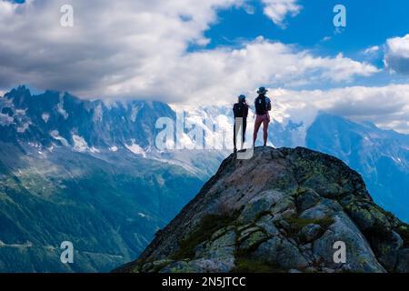 Zwei junge Wanderer stehen auf einem Felsen in der Nähe von La Flégère und blicken auf das Mont Blanc-Massiv. Stockfoto