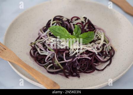 Gesunde Imitationsnudeln aus spiralförmigen Zucchini, verziert mit Basilikumblättern und garniert mit Parmesankäse und schwarzem Pfeffer auf Bambuspl Stockfoto