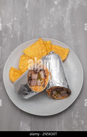 Mexikanischer Rindfleischburrito auf einem kleinen Teller mit Chips Nachos auf dem Teller Stockfoto