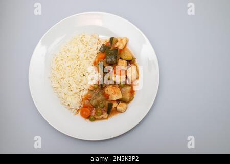 Tintenfischeintopf mit Gemüse und gekochtem Reis auf weißem Teller Stockfoto