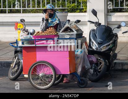 BANGKOK, THAILAND, FEBRUAR 04 2023, Eine Frau verkauft gegrilltes Fleisch an einem mobilen Verkaufsstand in einer Straße im Stadtzentrum Stockfoto