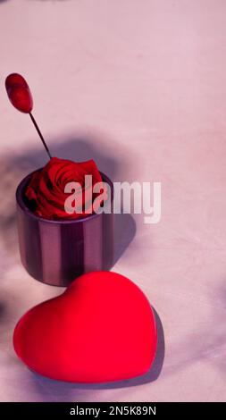 Vertikales Foto eines Herzens aus Schokolade mit einer kleinen Vase mit einer roten Rose und einem kleinen Herz. Kopierbereich, Produktfoto Stockfoto