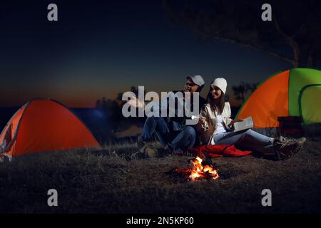 Ein Paar mit Taschenlampe in der Nähe des Lagerfeuers bei Nacht. Campingsaison Stockfoto