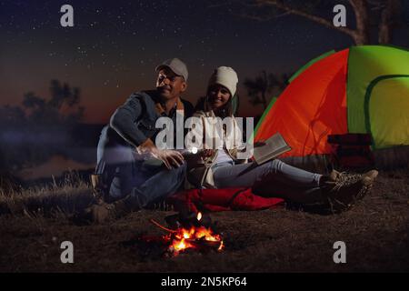 Ein Paar mit Taschenlampe in der Nähe des Lagerfeuers bei Nacht. Campingsaison Stockfoto